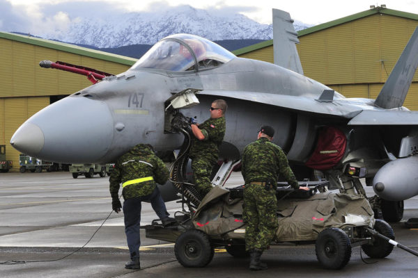 Des armuriers canadiens approvisionnent le canon d'un CF-188 Hornet, en arrière-plan on distingue le relief corse.