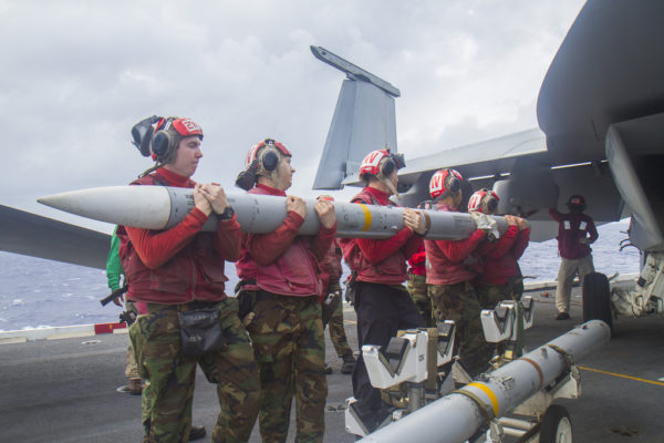 Des armuriers de l'US Navy installent un AMRAAM sur un Boeing F/A-18E Super Hornet en mer.